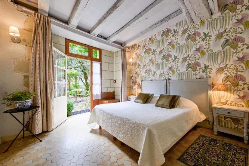Bedroom with white bedding, floral wallpaper, and open doors to a garden patio at Hôtel Diderot.