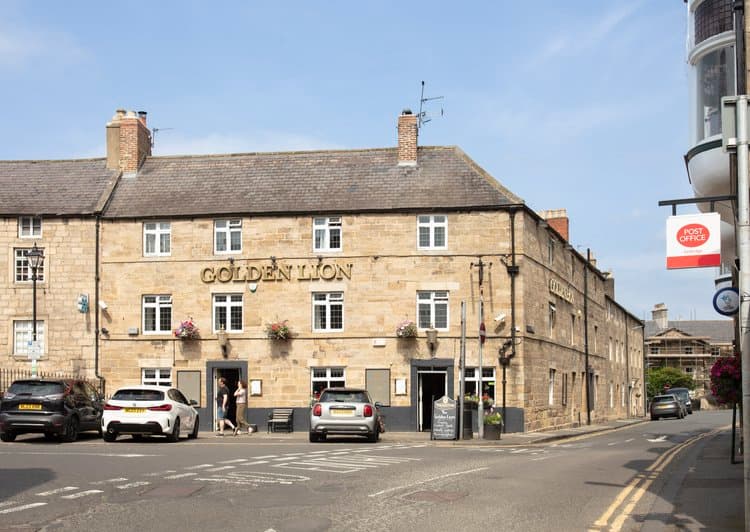 The Golden Lion pub made of stone on a street corner with parked cars.