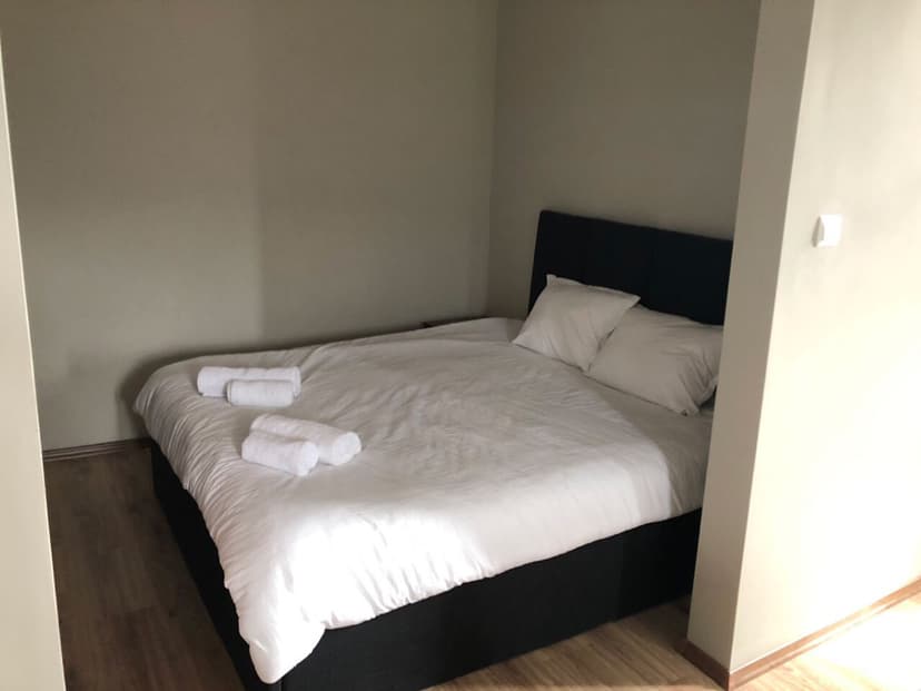 Double bed with white linens and rolled white towels in a simple room with light walls.