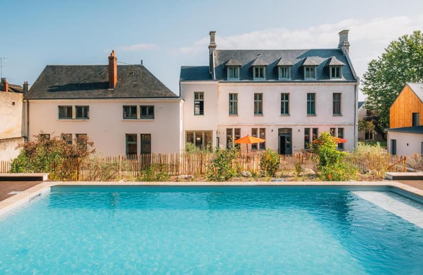 Swimming pool in front of white historic buildings with a wooden fence and orange umbrellas.