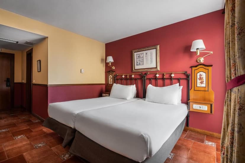 Twin beds with white linens against a red and yellow wall in a hotel room.