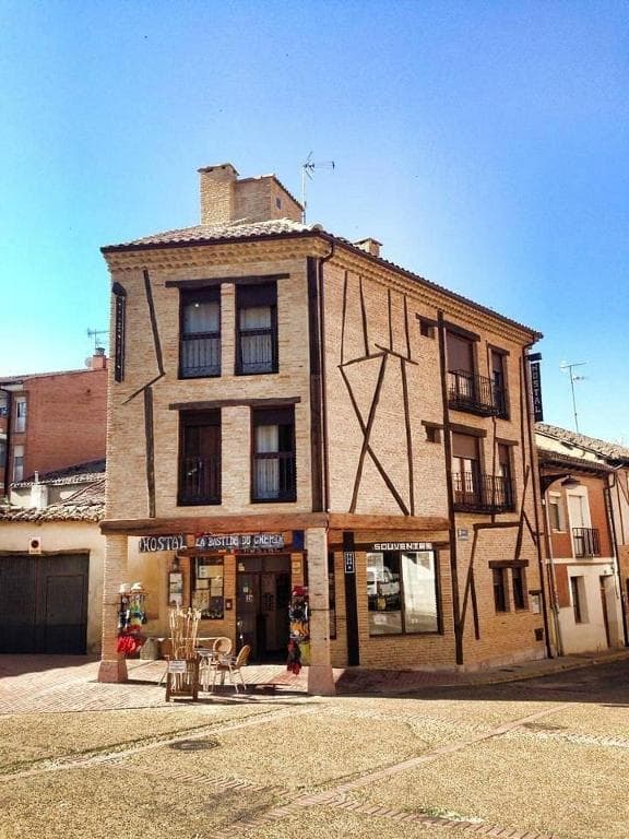 Hostal La Bistrot du Chemin and souvenir shop in a brick and timber-framed building under a clear blue sky.