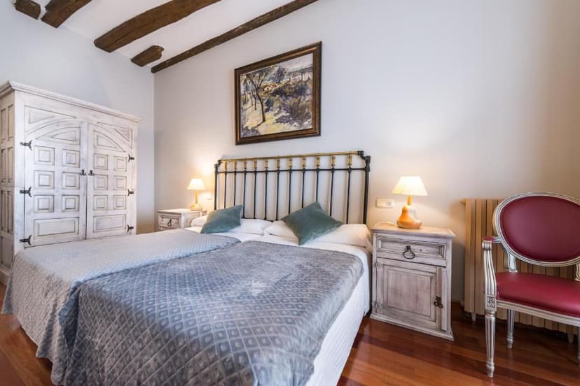 Twin beds with metal headboard, white distressed wardrobe, and exposed wood beams in Hotel Alda Vía León.