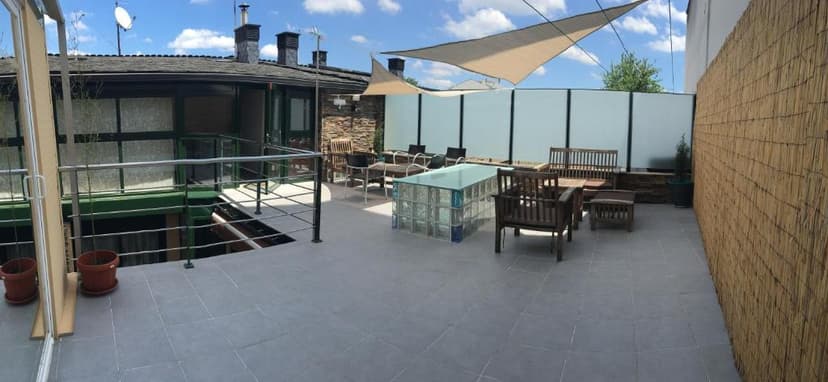 Rooftop terrace with outdoor seating, glass block table, and bamboo privacy screen under blue sky.