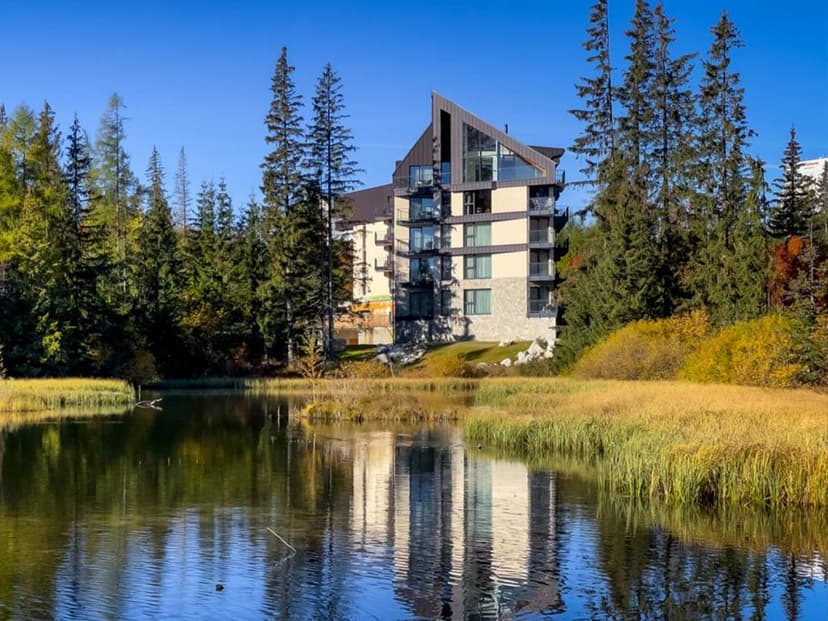 Modern resort building reflected in a calm lake surrounded by pine trees and autumn reeds