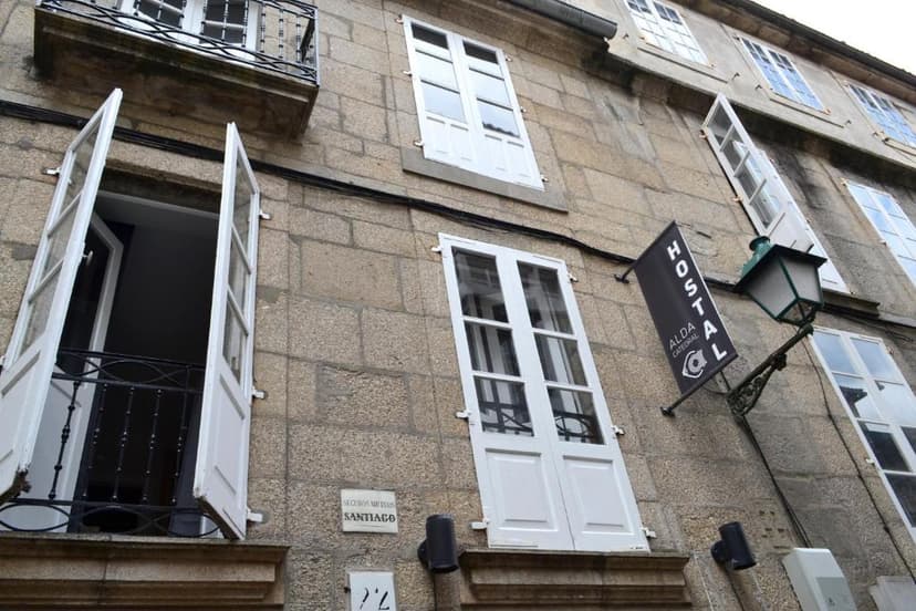 Stone building facade in Santiago de Compostela with white shuttered windows and a "Hostal Alda Catedral" sign.