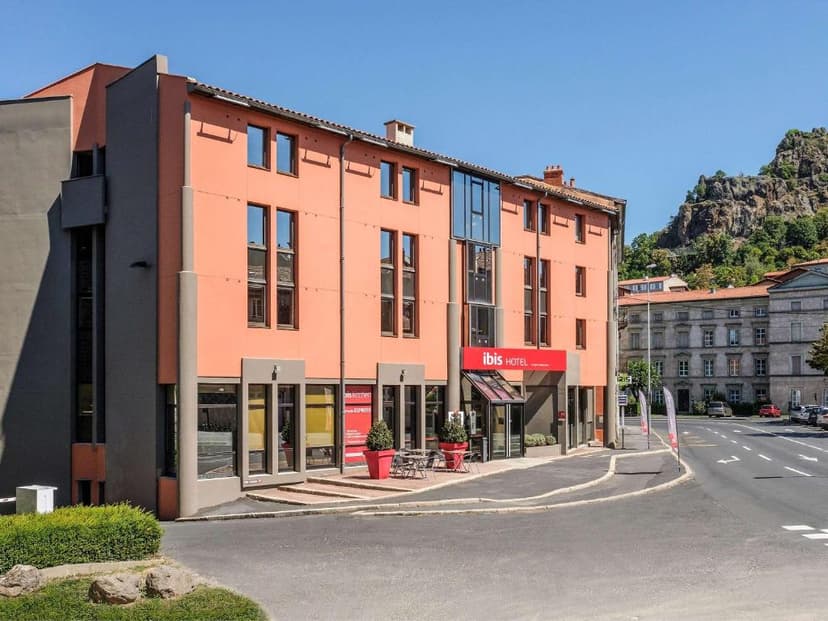 Ibis Hotel building in Le Puy-en-Velay with a rocky, tree-covered hill in the background.