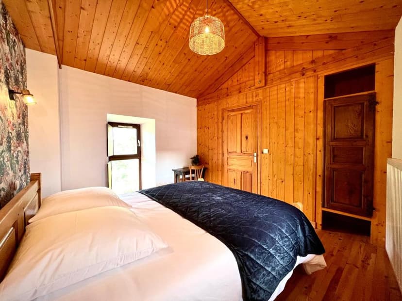 Bedroom with wood paneling, white bedding, and wicker pendant light in Gîte Le Nid d'Ange