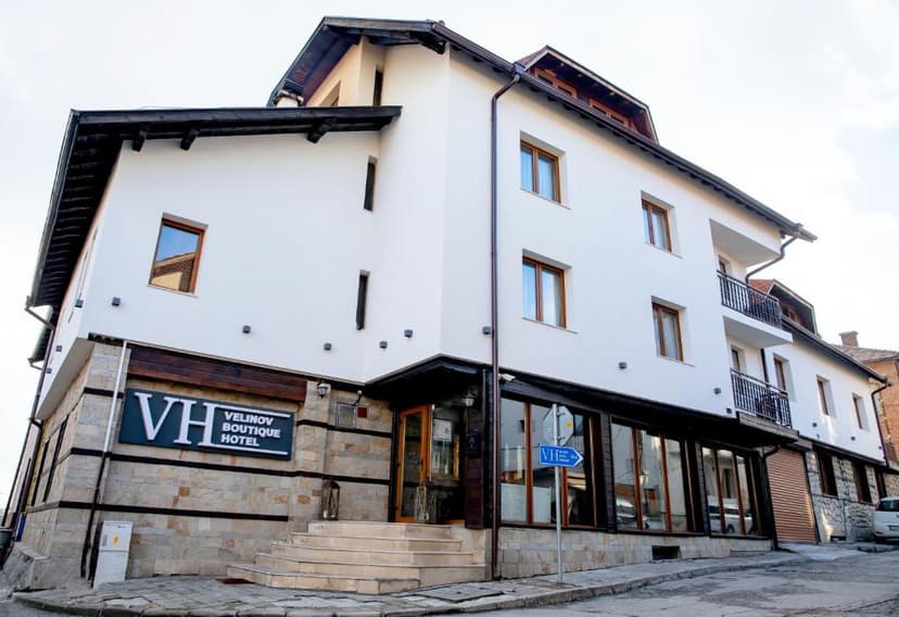Velinov Boutique Hotel exterior with white facade, stone base, and dark wood trim on a street.
