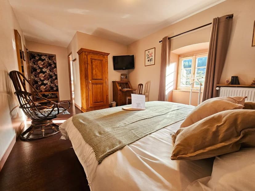 Bedroom with wooden furniture, wicker chair, and view of greenery through a window at Auberge de Chanteuges.