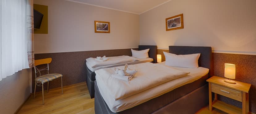 Twin beds with white linens and folded towels in a room with wooden floors, Spießberghaus.