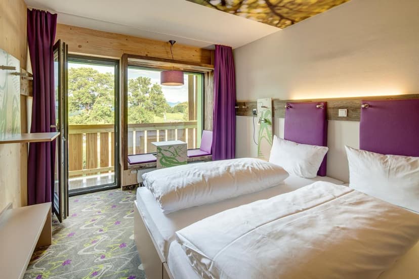 Hotel room with twin beds, purple accents, and balcony view of green trees in Berchtesgaden.