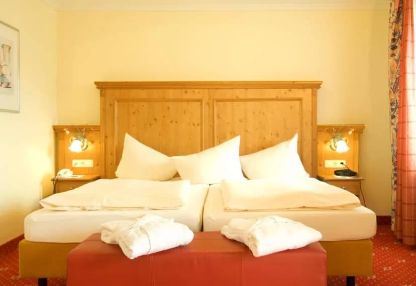 Alpenhotel Kronprinz hotel room with twin beds, wooden headboard, and white robes.