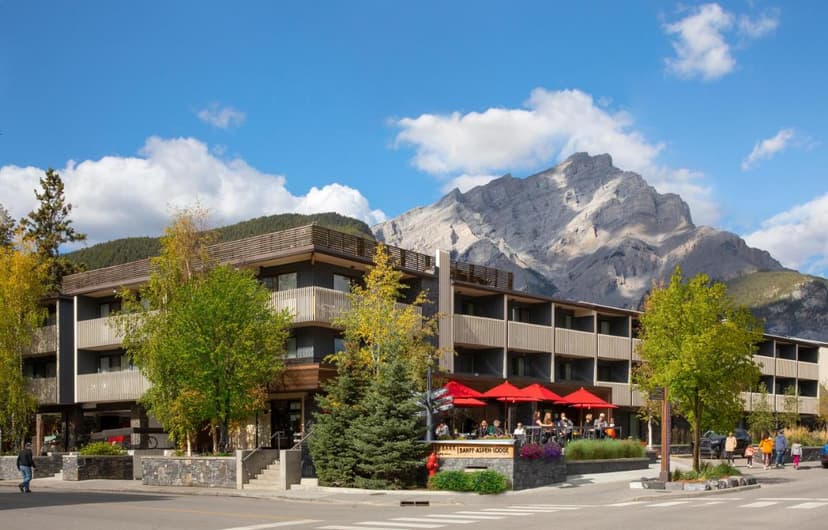 Banff Aspen Lodge with outdoor dining and large mountain backdrop under blue sky.