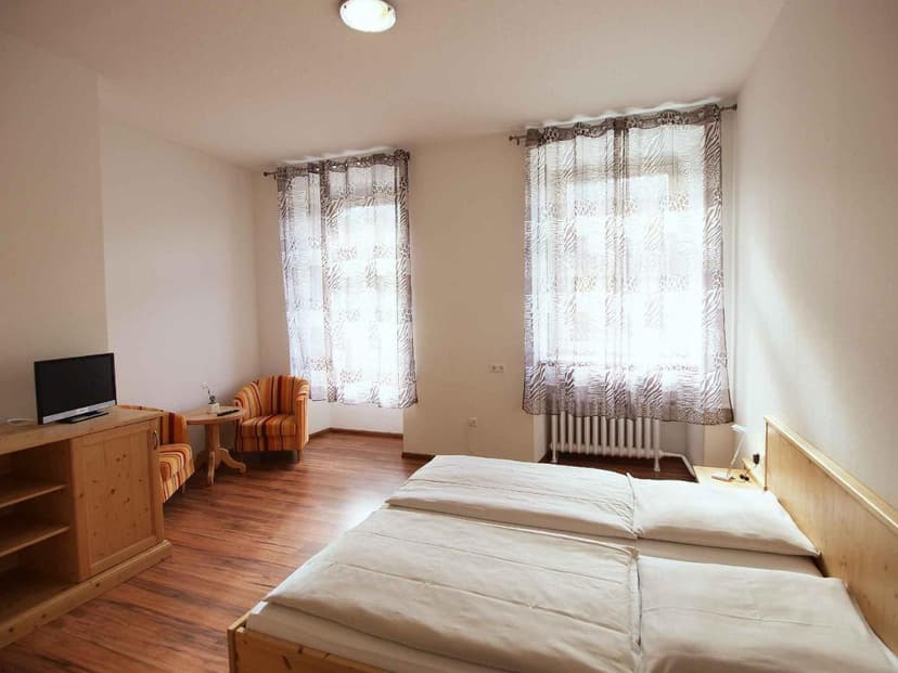 Hotel Klosterhof twin room with wood furniture, striped armchairs, and sheer patterned curtains.