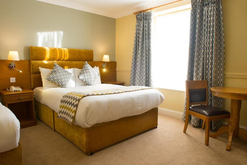 Hotel room with large bed, yellow headboard, patterned pillows, and bright window in Tralee.