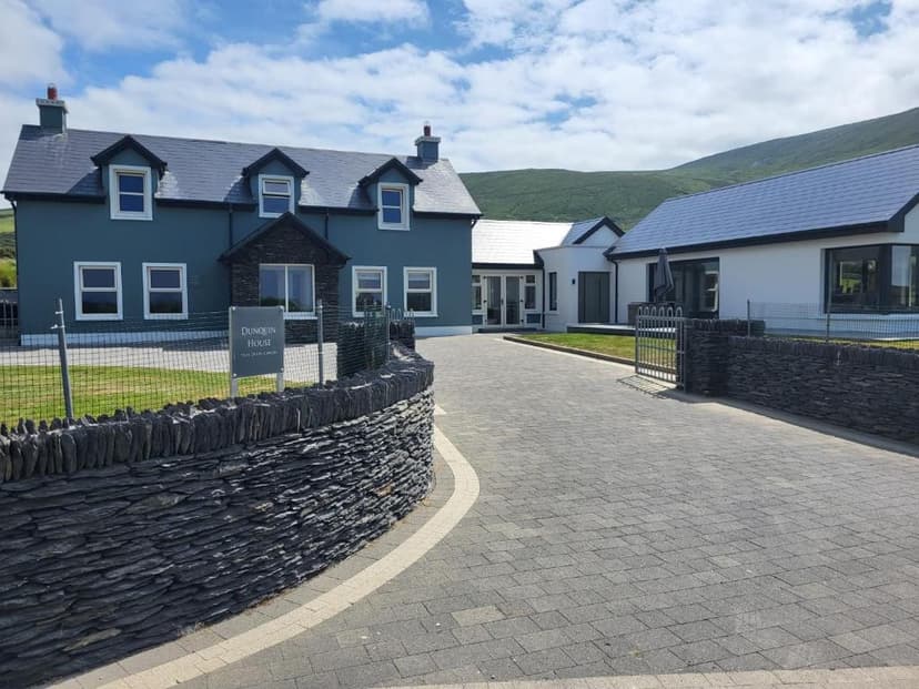 Dunquin House with slate wall entrance and green hills in background under blue sky.