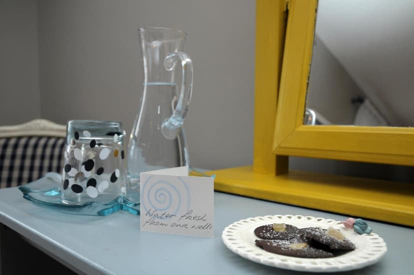 Water carafe, polka-dot glass, and chocolates on a table near a yellow mirror frame.