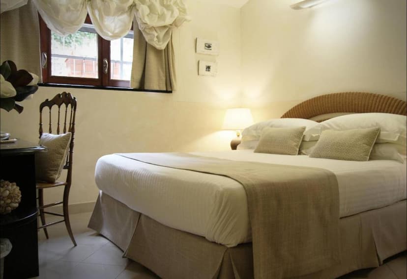 Bedroom with large bed, wicker headboard, and window with draped curtains at Locanda A Cà Du Gigante.