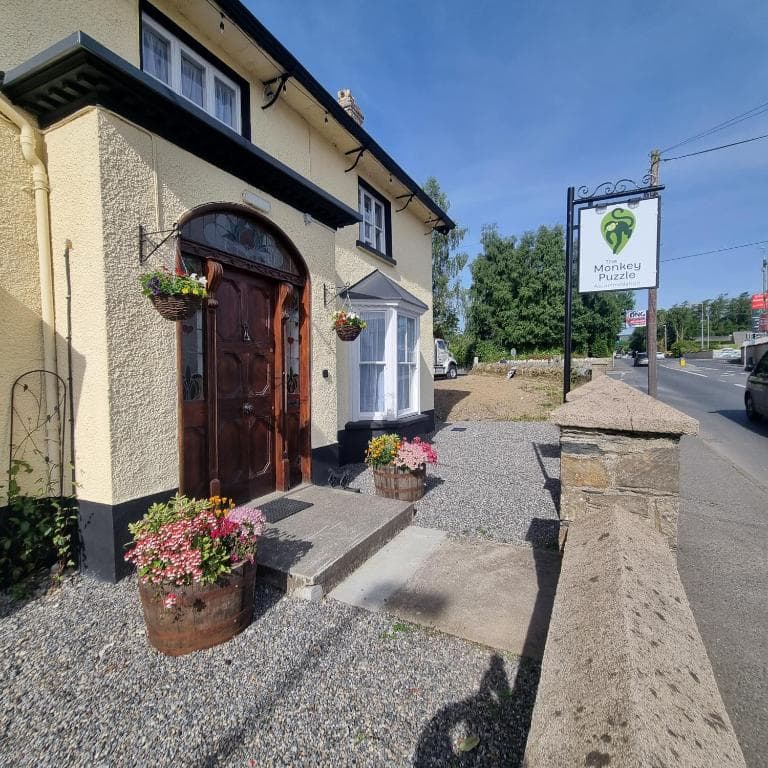Yellow building entrance with "The Monkey Puzzle" sign next to a road on a sunny day.