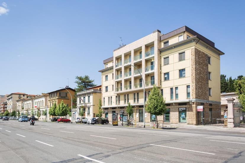 Apartment building facade along a wide city street with parked cars and clear blue sky.