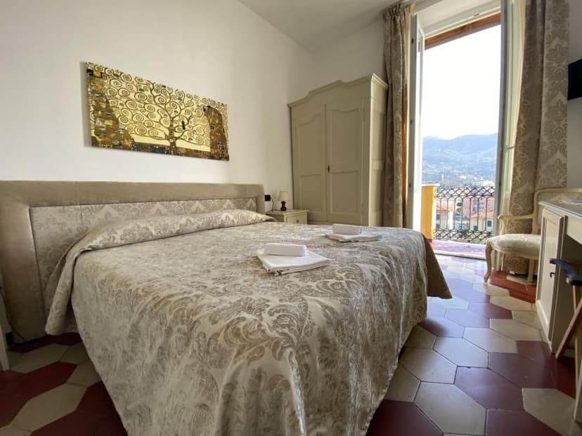 Bedroom with patterned bedding, Klimt-style art, and balcony view of hillsides.