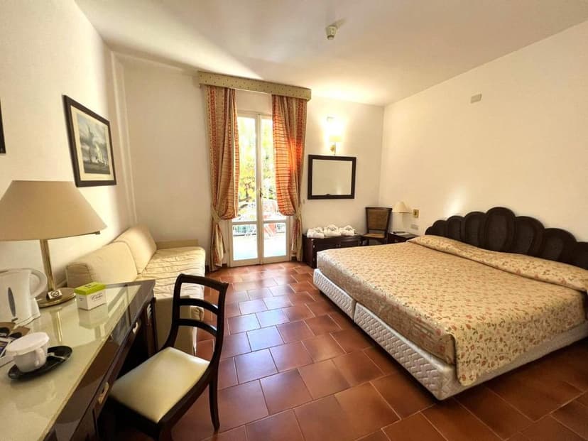 Hotel room with large bed, desk, sofa, and balcony doors with patterned curtains