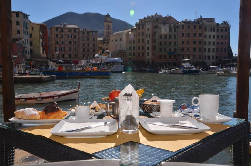 Breakfast setting overlooking harbor with colorful buildings and mountains, filename I-Tre-Merli-Locanda.jpg