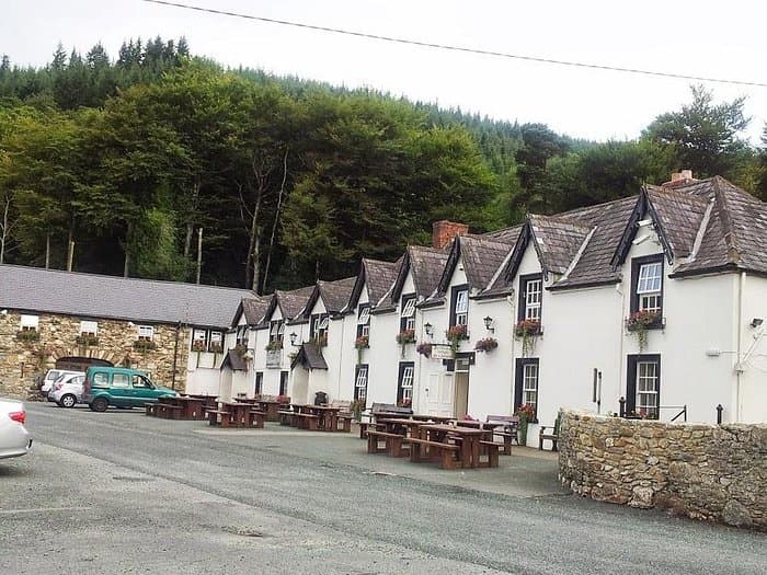Glenmalure Lodge building with outdoor picnic tables against a backdrop of dense green forest.