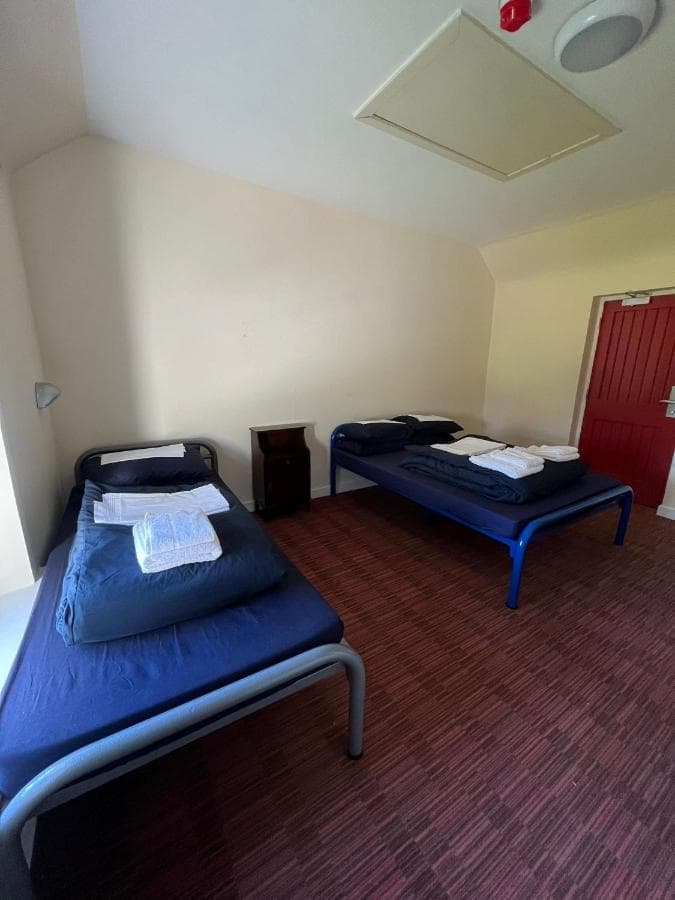 Twin beds with blue bedding in a simple hostel room with a red door, Knockree Hostel.