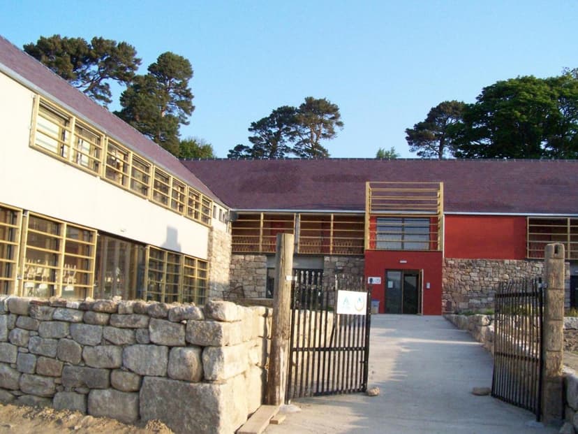 Knockree Hostel building with stone walls, large windows, and open metal gates under a clear blue sky.