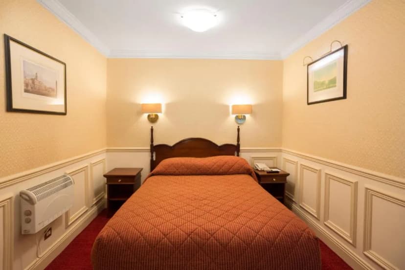 Cozy hotel room with double bed, bedside tables, wall art, and white paneling.