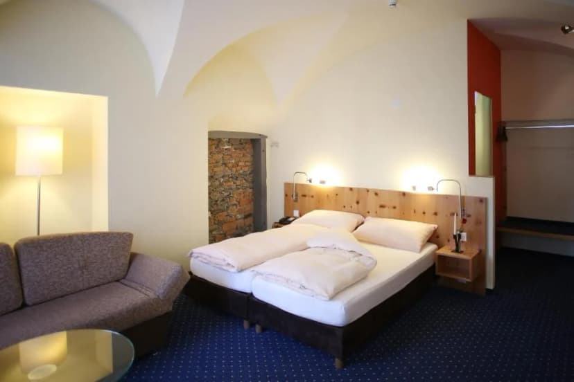 Hotel room with twin beds, wood headboard, sofa, and exposed brick doorway in Ambiente Hotel Freieck.