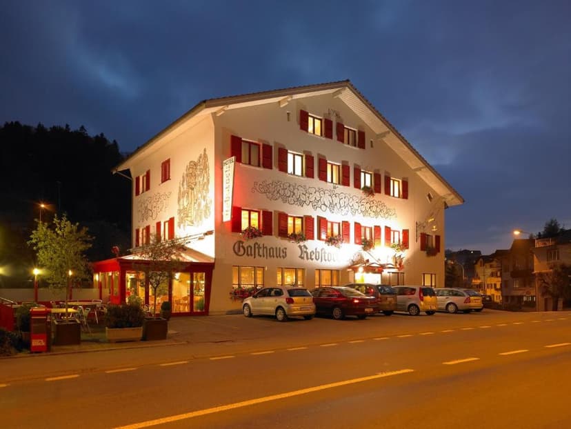 Gasthaus Rebstock hotel illuminated at night with parked cars in front and dark hillside backdrop.