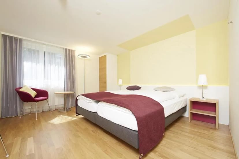 Hotel Rebstock twin room with light wood floors, yellow accent wall, and burgundy throw.