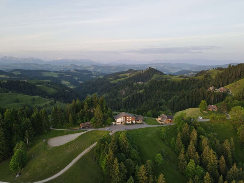 Hotel complex nestled in rolling green hills with distant snow-capped mountains visible.