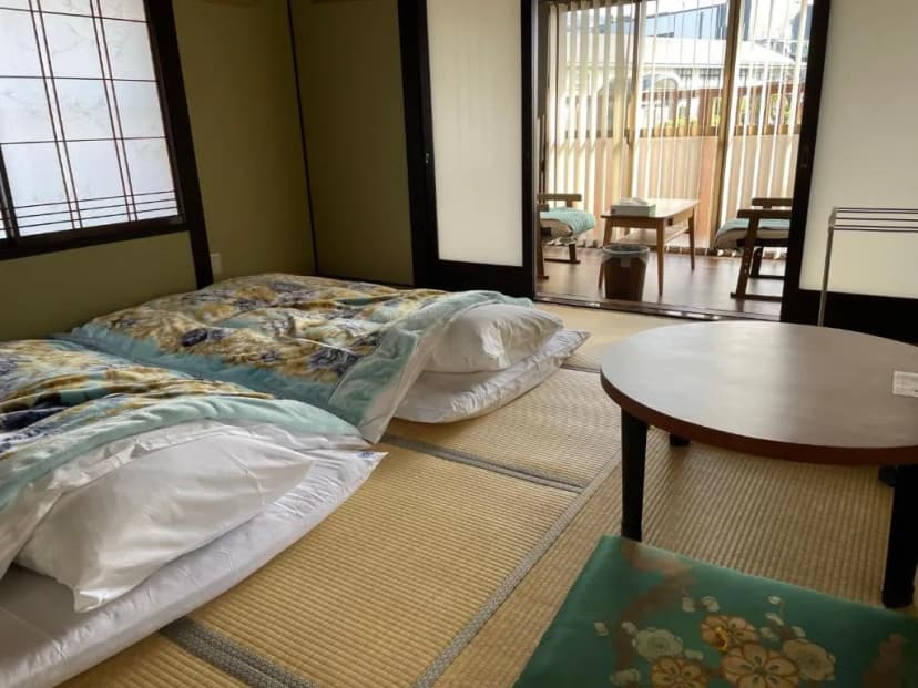 Japanese style room with futons on tatami mats, low table, and sliding door to balcony in Matsumoto