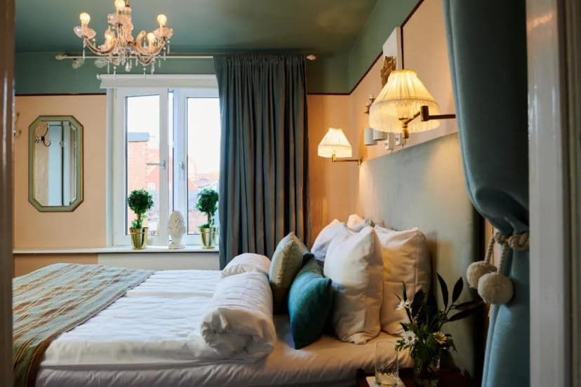 Hotel room at Hotell Bäckagården with chandelier, window, and plush bedding.