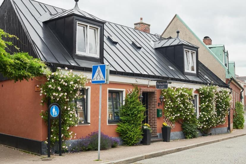 Hotell Bäckagården building with salmon-colored walls, black roof, and climbing white roses.