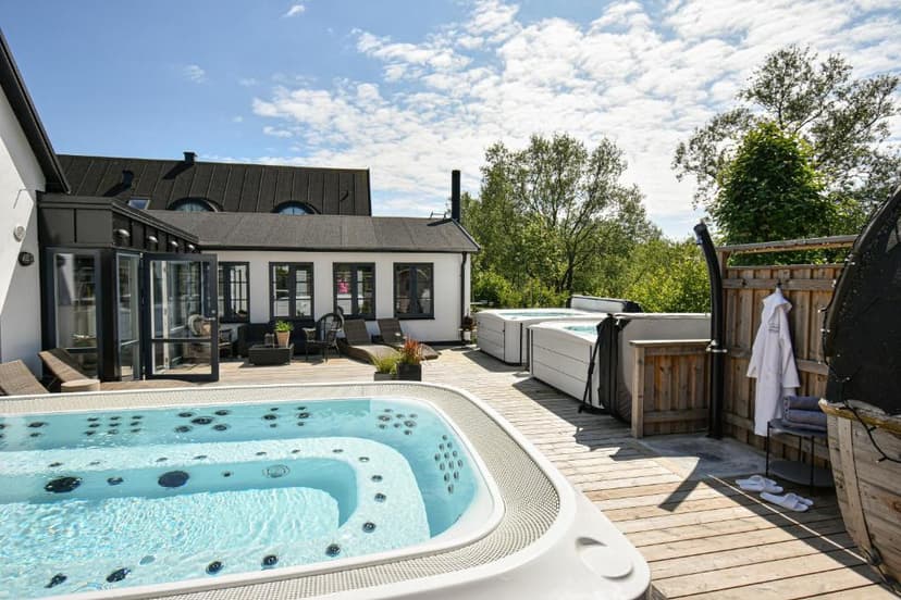 Outdoor spa deck with hot tubs, lounge chairs, and white building at Kåseberga Gårdshotell & Spa.