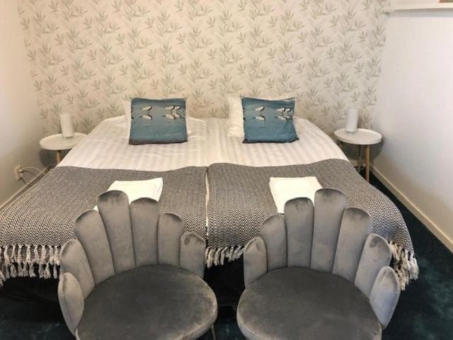 Twin beds with decorative pillows, gray scallop chairs, and leaf-patterned wallpaper in Skillinge room.