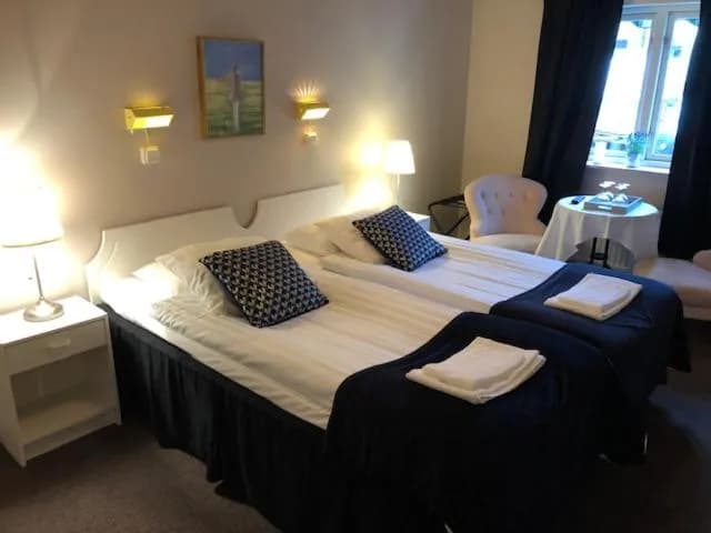 Twin beds with white linens and dark blue throws in a hotel room at Hotell Turistgården i Simrishamn.