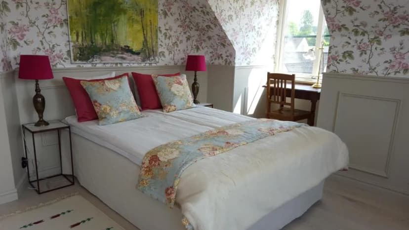 Bedroom at Brösarps Gästgifveri & SPA with floral wallpaper, white bedding, and bright window light.