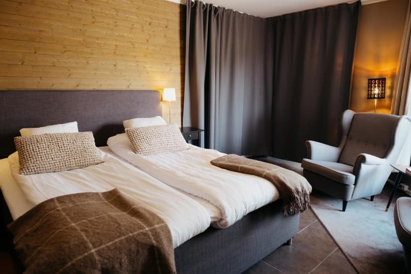 Twin beds with white linens and brown throws in Abisko Mountain Lodge room with wood wall.