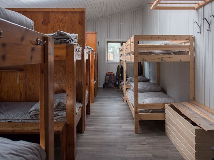 Wooden bunk beds line a simple room with white paneled walls, referencing Abiskojaure.