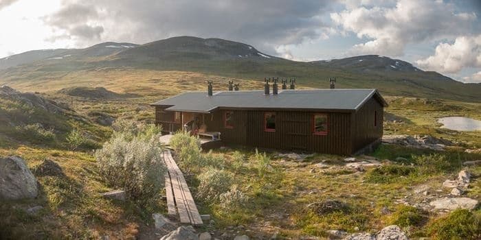 Alesjaure hut in a vast, grassy mountain landscape with a wooden boardwalk.