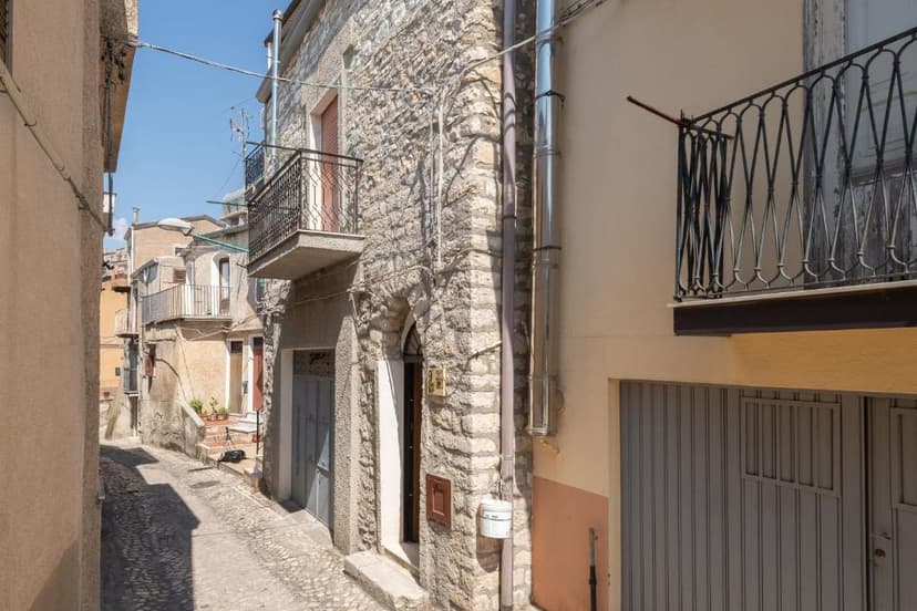 Narrow cobblestone alleyway between stone and stucco buildings with balconies under a clear sky.