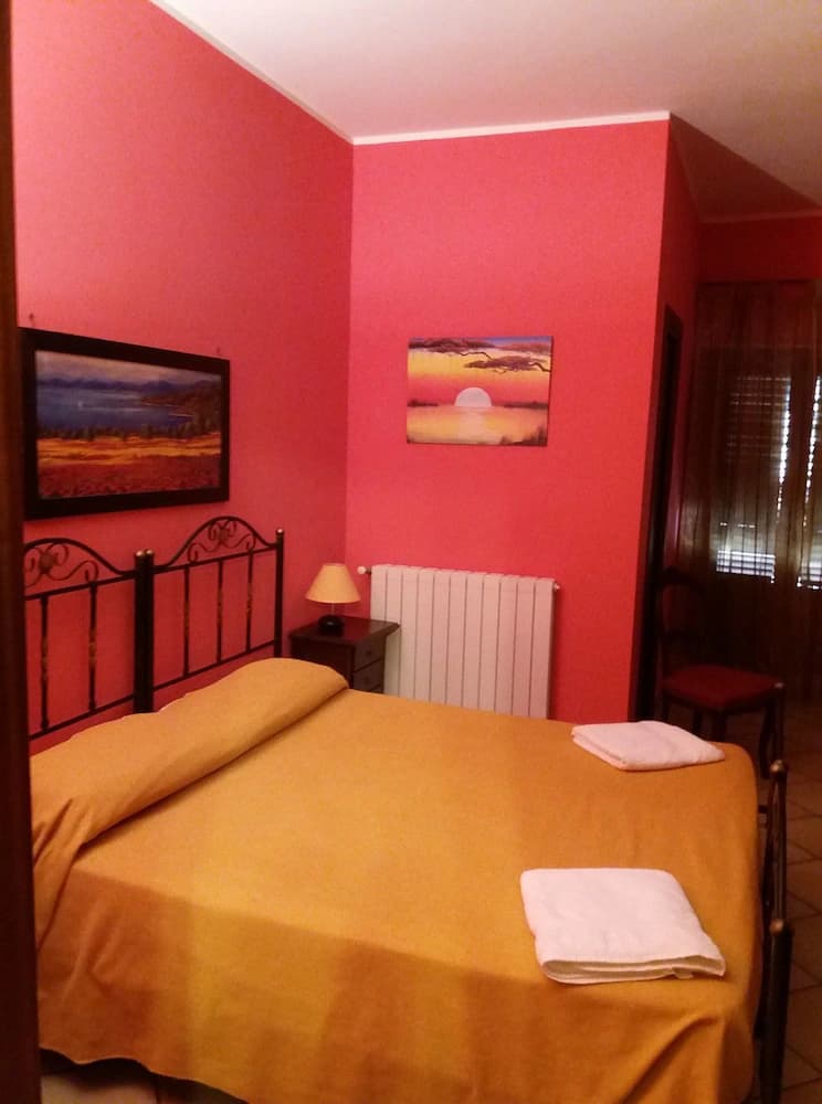 Bedroom with bright pink walls, yellow bedding, black metal headboard, and landscape paintings.