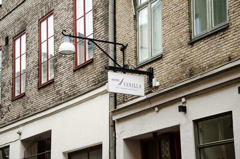 Hotel Vanilla hanging sign on weathered brick building facade with red-framed windows