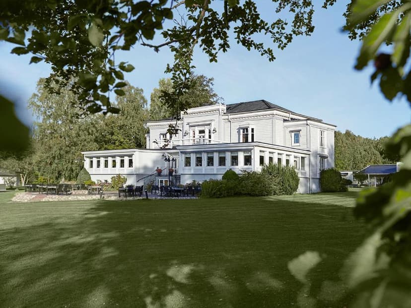 Aspenäs Herrgård manor house with outdoor dining area and large green lawn framed by trees.